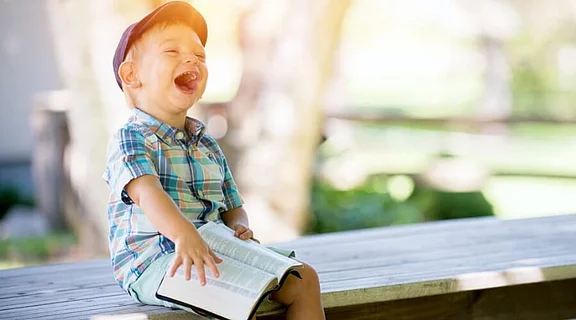 ein lachendes Kleinkind auf einer Holzbank